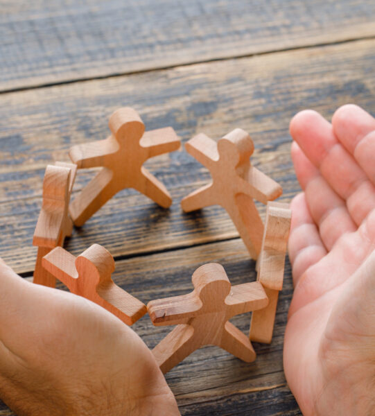 Business success concept on wooden background high angle view. hands protecting wooden figures of people.