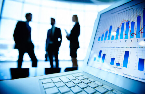 Financial document in laptop on background of three business partners interacting