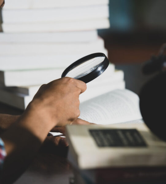Educational theme: Close -up Student looking through a magnifying glass to  book